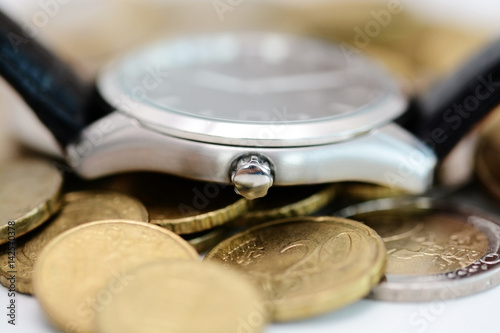 Watch on pile of coins suggesting that time is a valuable resource