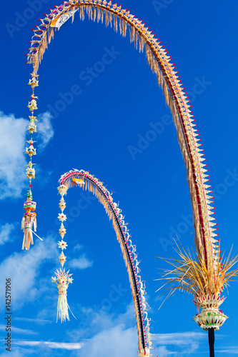 Traditional Bali Penjor, bamboo pole with decoration on village street in front of Balinese people house and temple on Galungan, Kuningan Hindu holidays. Indonesian art and culture. Travel background photo