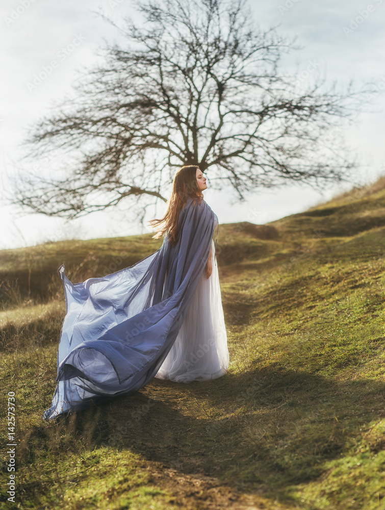 A big, beautiful woman in a blue raincoat, walks in a fog. Background dark forest, bare trees. Creative colors A big, beautiful woman in a blue raincoat, walks in a fog. Background dark forest, bare trees. Creative colors