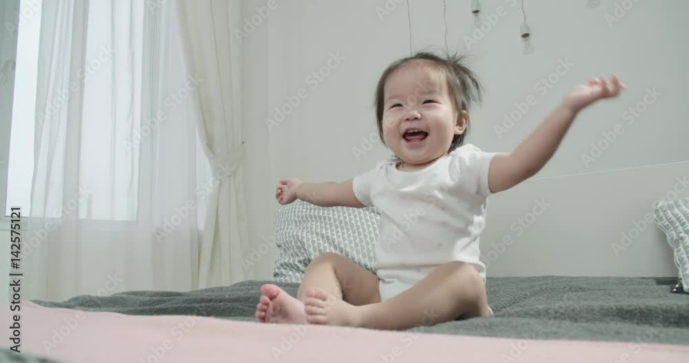 little Asian girl 1 year,having fun on the bed in the room , emotionally expresses joy
