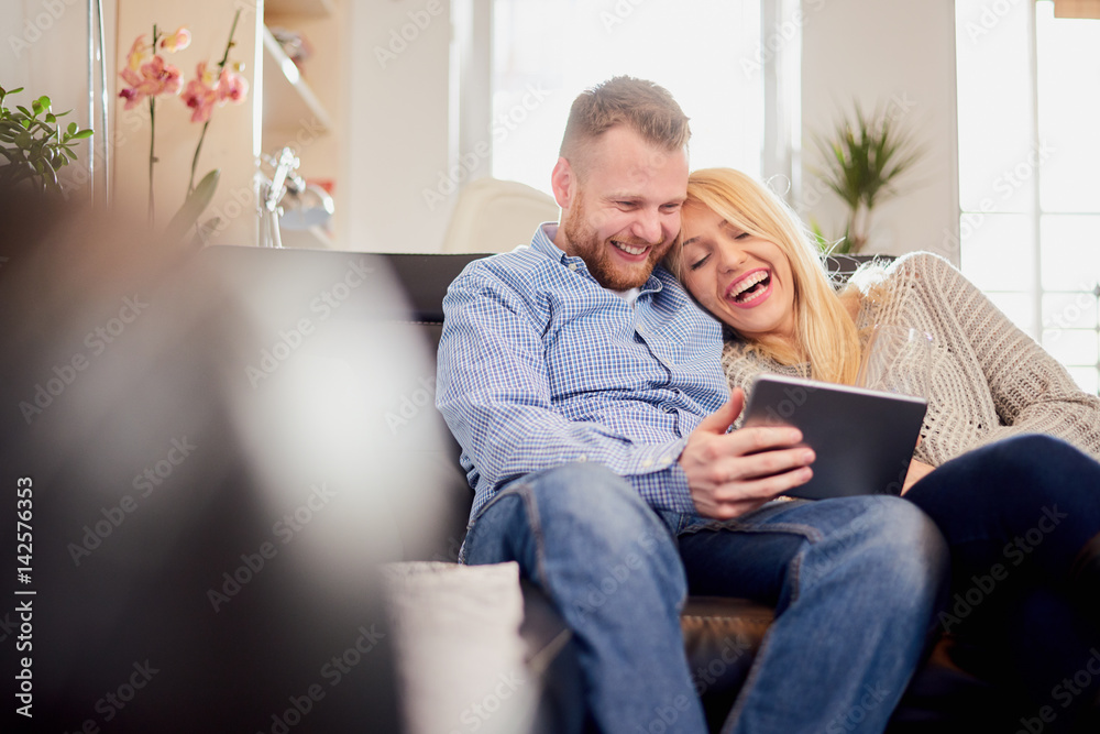 Happy couple sitting on sofa and looking at tablet