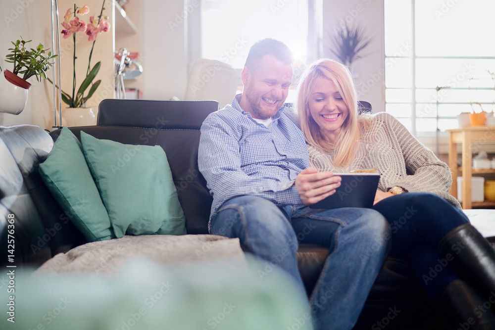 Caucasian happy couple using tablet computer while sitting on sofa in living room Caucasian happy couple using tablet computer while sitting on sofa in living room