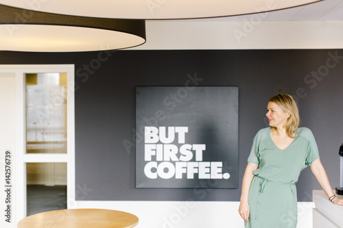 A woman stands in front of a coffee corner at work.
