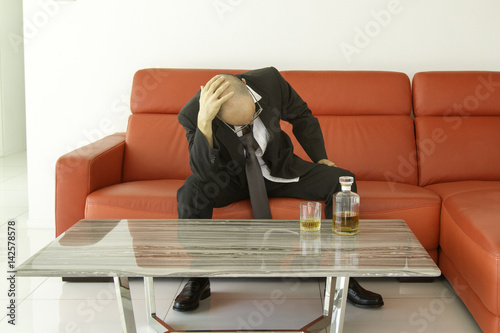 Fotografie Desperate and depressed man with black suit spending time with bottle of whiskey
