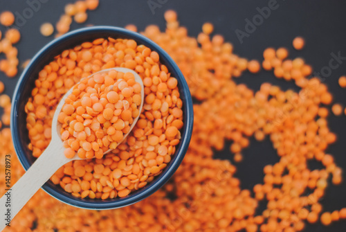 Red lentil in bowl with spoon on black background