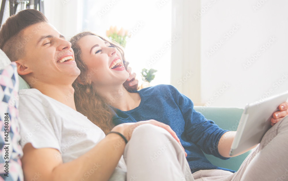 Couple on sofa at home using digital tablet and laughing
