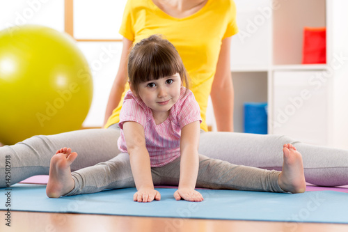 Mother and daughter kid doing sport exercises. Child bending down stretching with hands to floor.