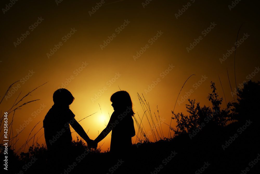 Silhouettes of a boy and a girl holding hands while walking in nature ...