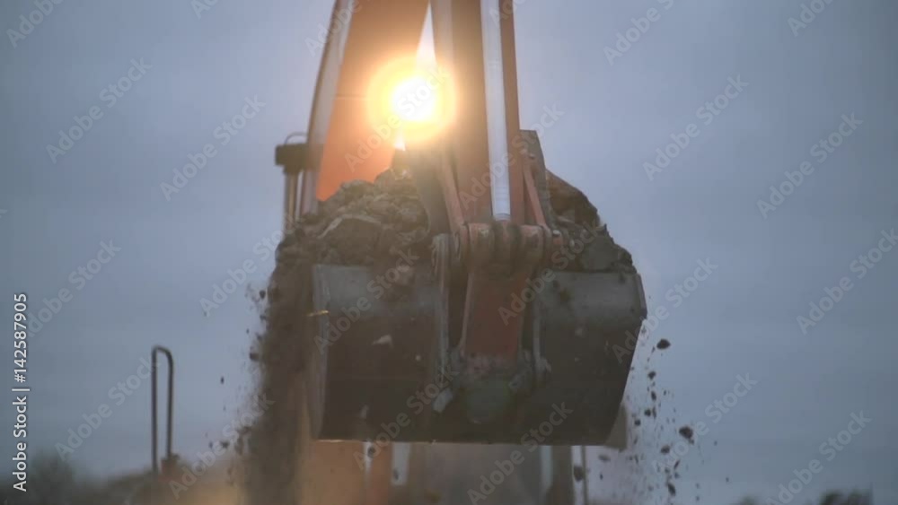 Excavator transports ground at night.Soil falling out of scoop. Construction excavator digging in the ground at construction or job site. Slow motion shot.Heavy machinery,industrial equipment concept.