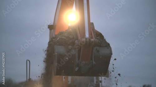 Excavator transports ground at night.Soil falling out of scoop. Construction excavator digging in the ground at construction or job site. Slow motion shot.Heavy machinery,industrial equipment concept. photo