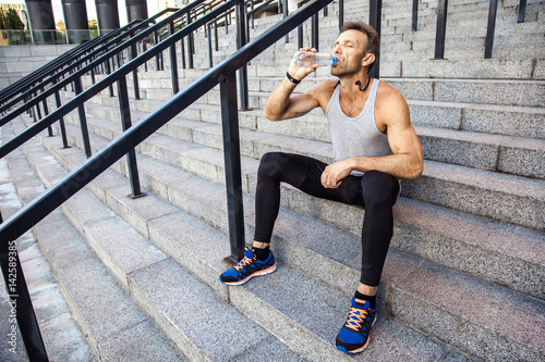 Thirsty sportsman take a rest and drinking water after running. fitness, sport, exercising and people healthy lifestyle concept.