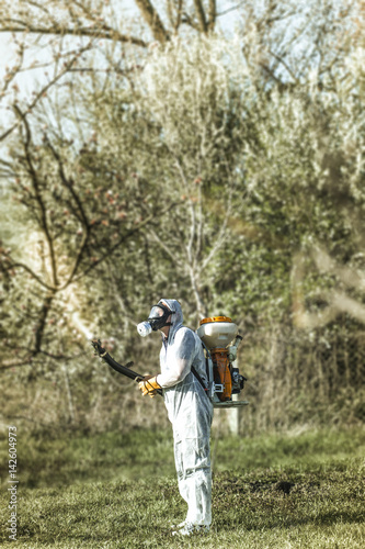 Young farmer spraying apricot trees with chemicals in the orchard