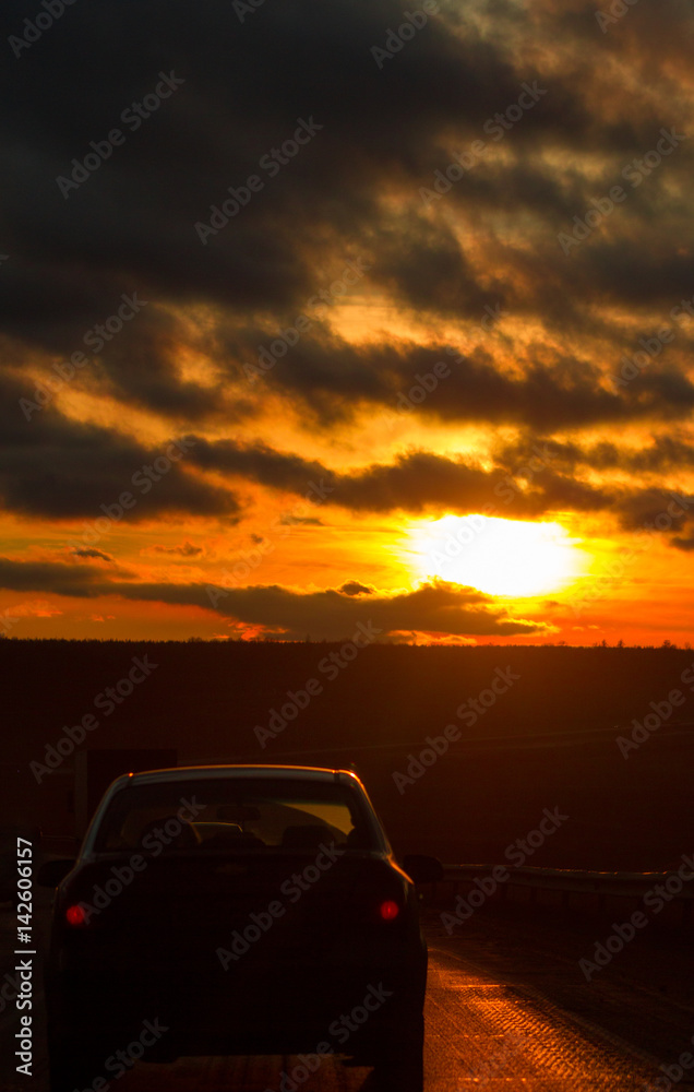 Highway road and car in front of orange sunset sky at winter