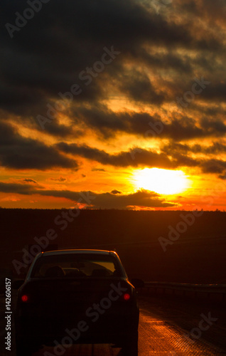 Highway road and car in front of orange sunset sky at winter