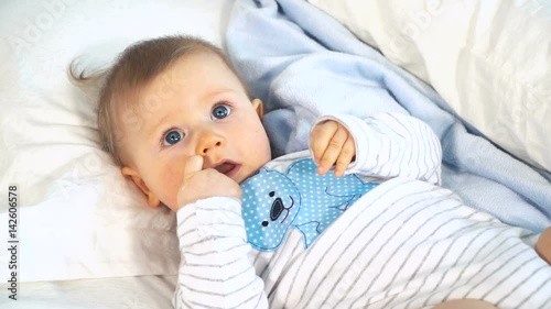 baby mit großen blauen augen und blonden haaren im bett