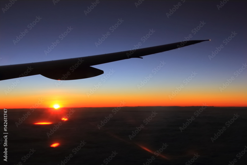 Airplane wing in flight, warn and cold colors through from window, beautiful sunrise light Airplane wing in flight, warn and cold colors through from window, beautiful sunrise light