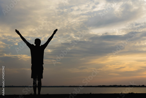 Silhouette of a man with hands raised in the sunset.