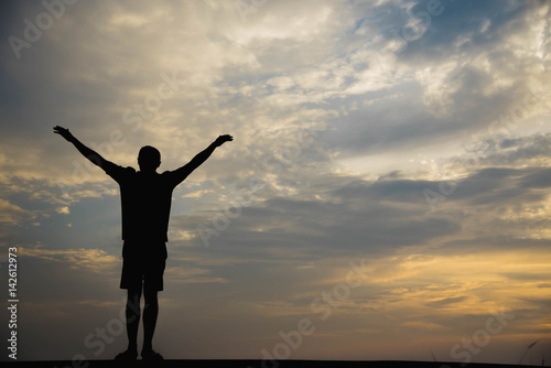 Silhouette of a man with hands raised in the sunset.