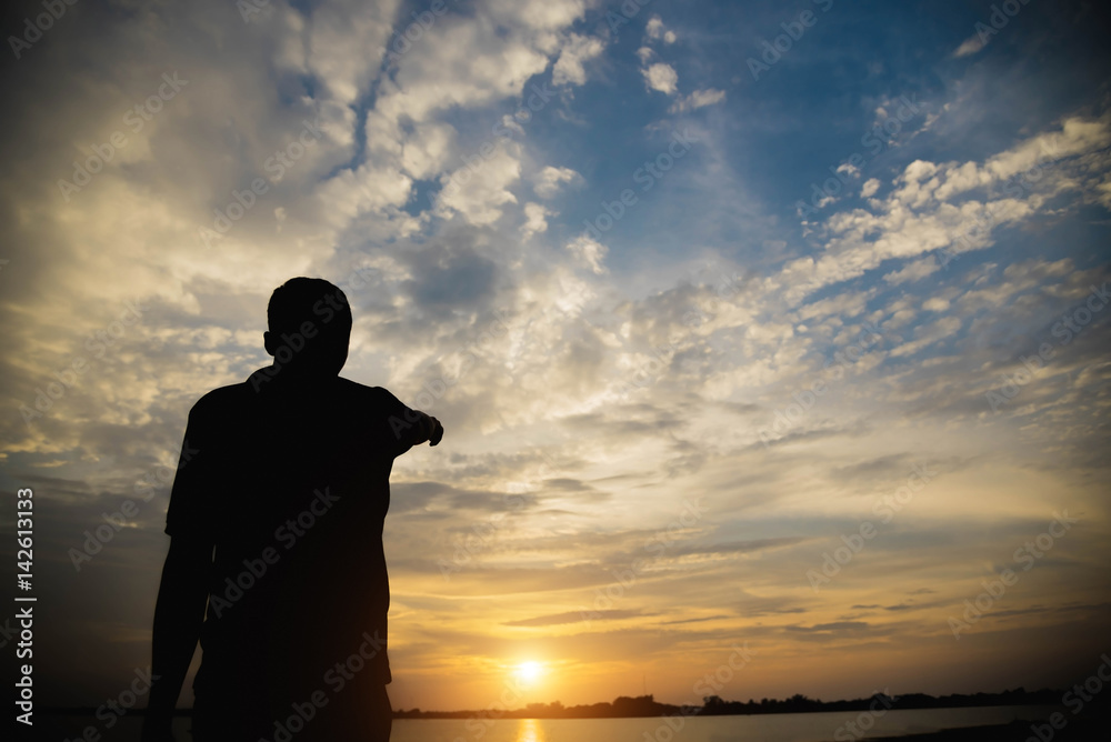 Fototapeta premium Silhouette of a man with hands point to sky in the sunset.