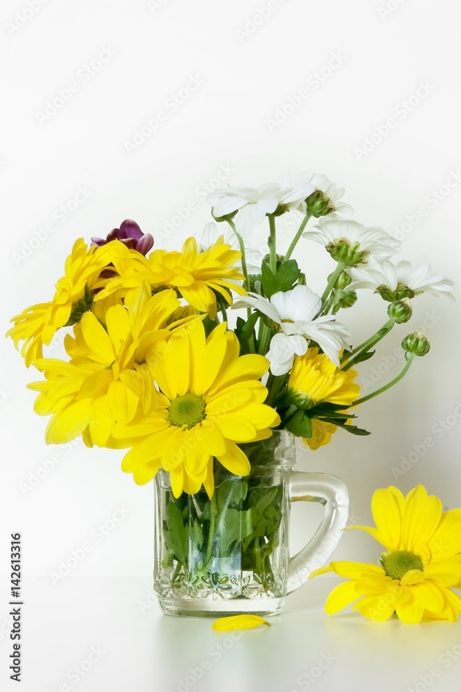 Beautiful bouquet of yellow and white chrysanthemum in little glass cup with a handle, used as a vase, on white background. Spring concept. 