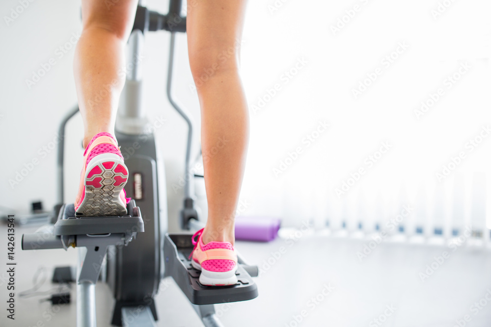 Naklejka premium Young woman's muscular legs on stepper/treadmill, closeup