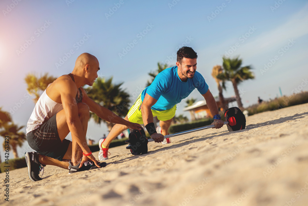 Muscular man doing push ups at beach in morning. Training hard