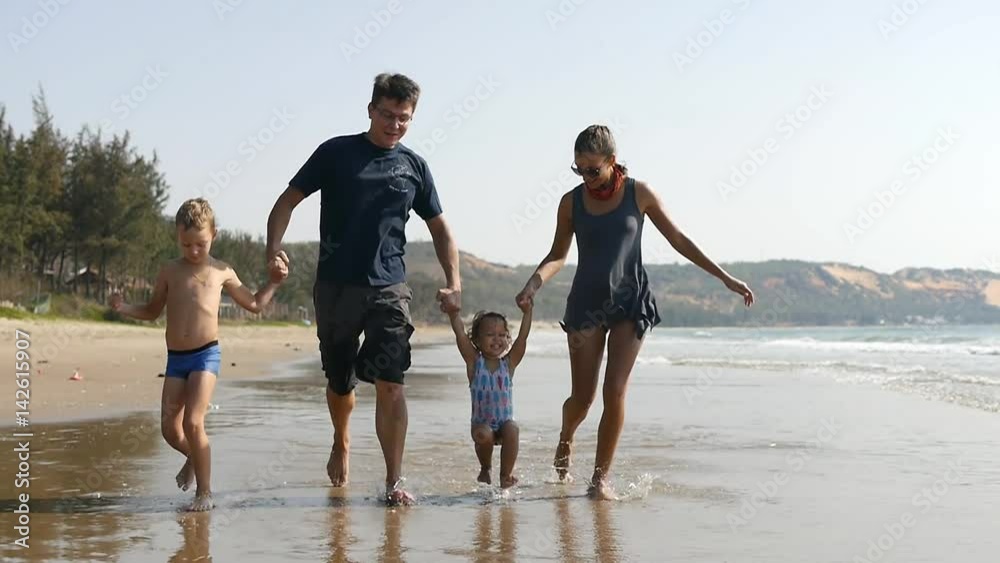 Happy healthy family having fun on summer vacation. Running along the beach splashing the water. Lifting daughter by hands on the seashore. Slow motion 50Fps. Happy healthy family having fun on summer vacation. Running along the beach splashing the water. Lifting daughter by hands on the seashore. Slow motion 50Fps.