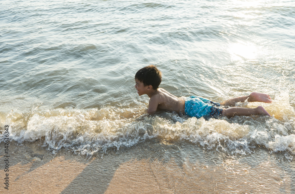 happy asian boy playing in the water waves at sea ocean
