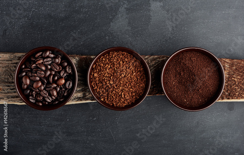 Three kinds of coffee: beans, milled, instant in cups on wooden plank.  photo