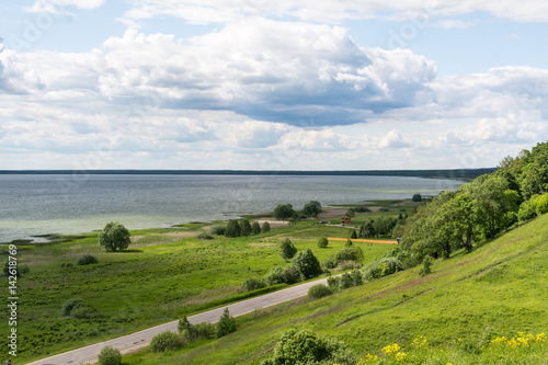 Lake, empty road, hill and plain. Stormy clouds and horizon on background. Romantic deserted landscape of middle Russia.