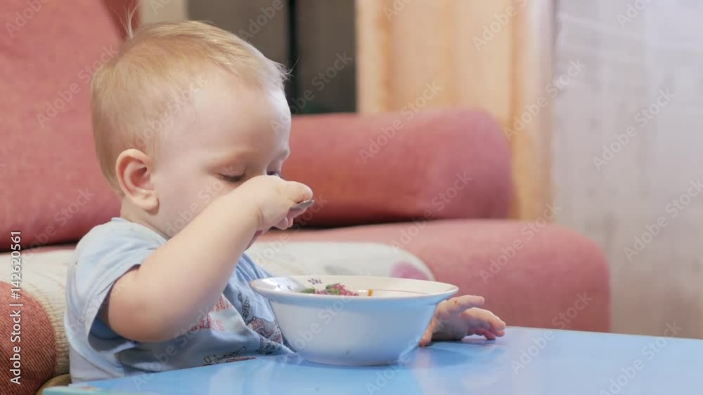 An attractive boy 2 years old is eating red soup himself. Spoon and hands flowing liquid. The concept of healthy eating of children. An attractive boy 2 years old is eating red soup himself. Spoon and hands flowing liquid. The concept of healthy eating of children.