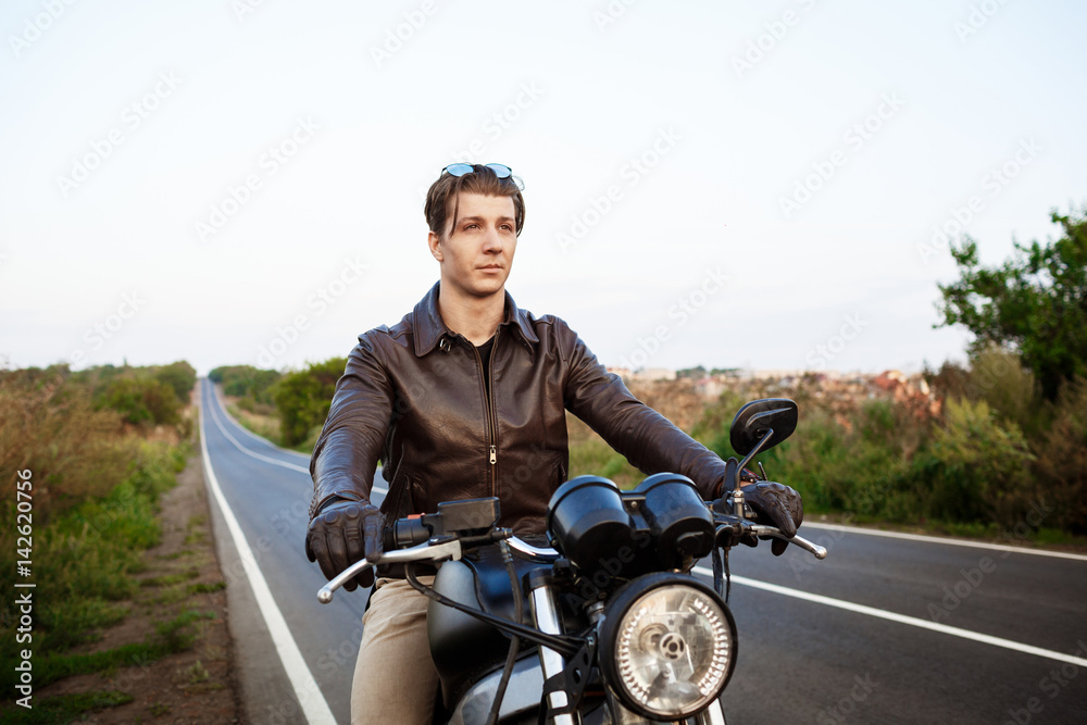 Young handsome man riding on motorbike at countryside road.