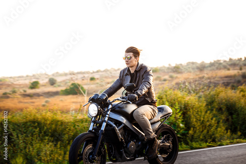Young handsome man riding on motorbike at countryside road.