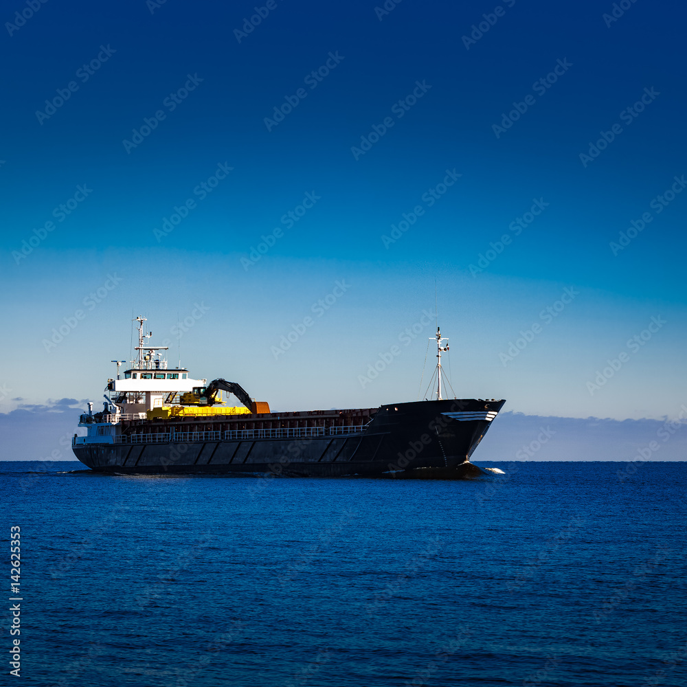 Black cargo ship with long reach excavator moving by baltic sea