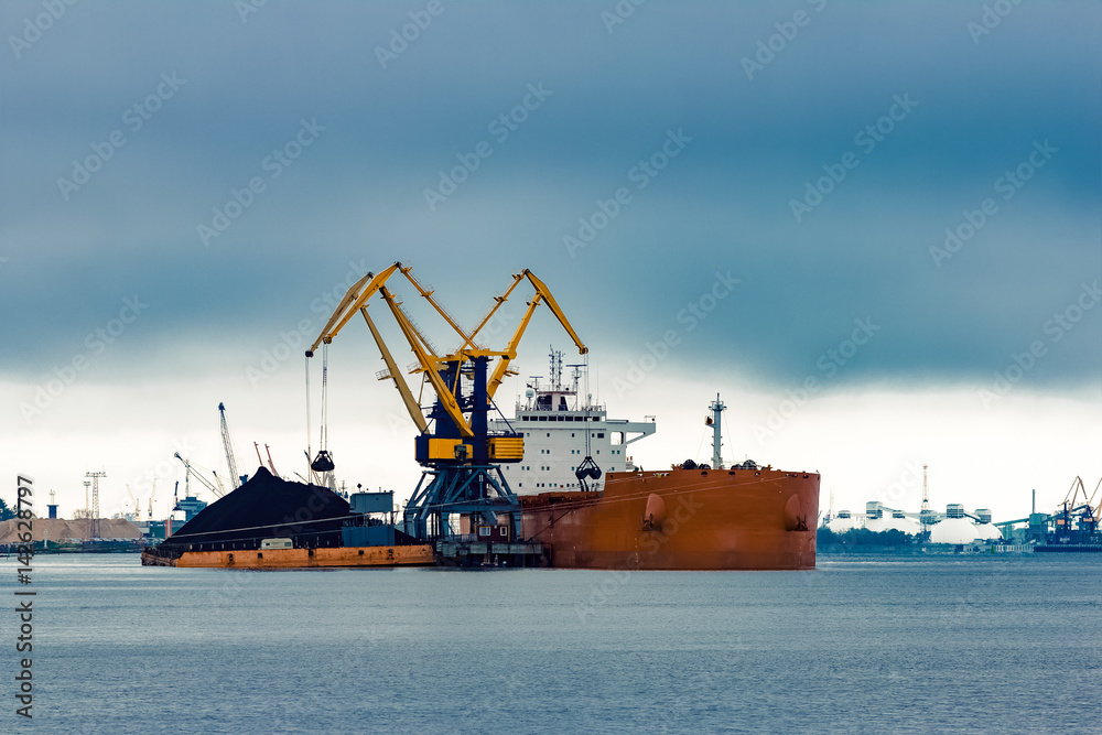 Large orange cargo ship loading with a coal in the port