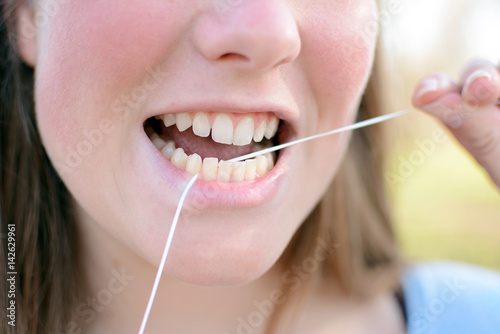 Portrait of beautiful young woman cleaning her teeth with dental floss.