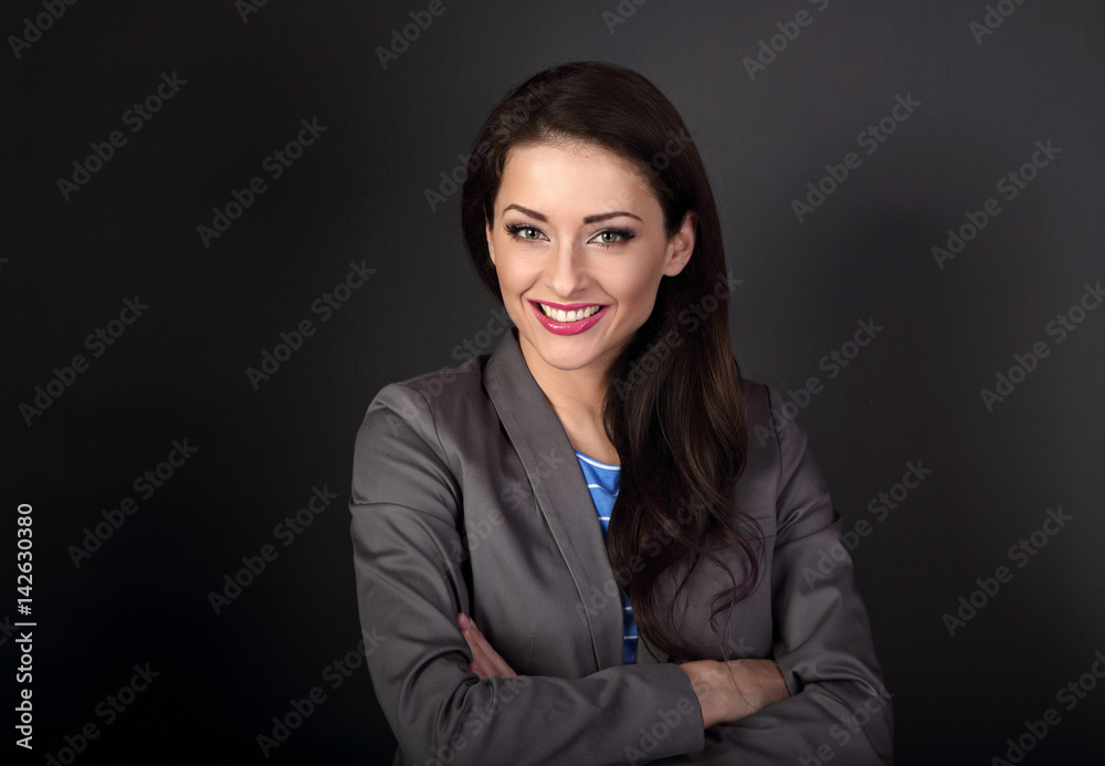 Beautiful toothy smiling business woman in grey suit looking happy with folded arms on dark grey background with empty space