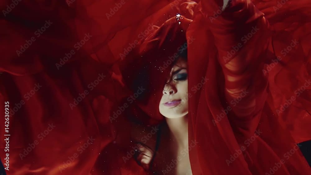 a young woman in a red dress swimming under water like in a fairy tale