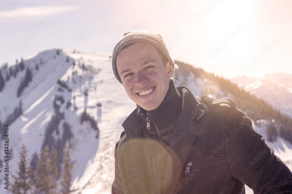 young man standing in the sun surrounded by snowy mountains