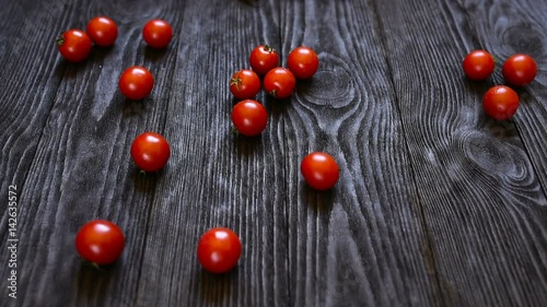 Cherry tomatoes roll over the screen in slow motion on wooden background