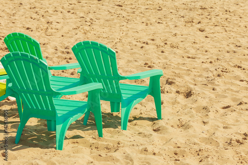 Green plastic chairs on sand.