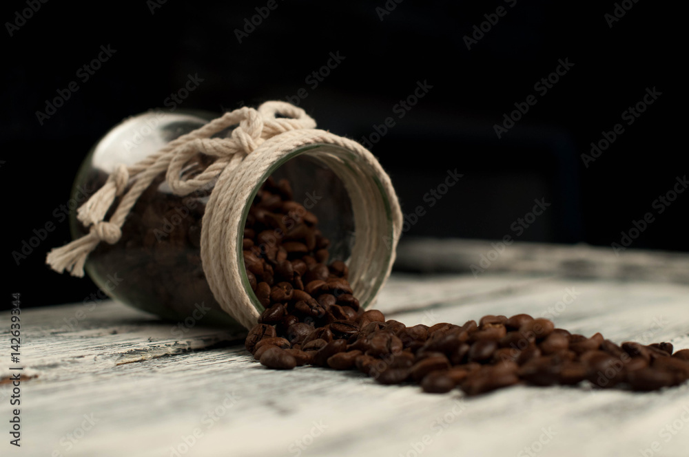 scattered coffee beans in a jar on wood