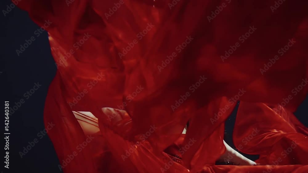 a young woman in a red dress swimming under water like in a fairy tale
