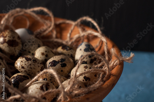 quail eggs in wooden bowl isolated on blue background close up