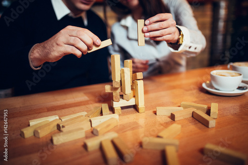 at the coffee shop hands on the table folded puzzle. Play jenga on the table, wooden tol, couple plays photo