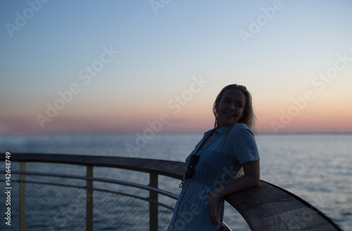 Woman enjoying her free time on the moll on the beach at the sunset time. Sillouette of a woman on a sunset.