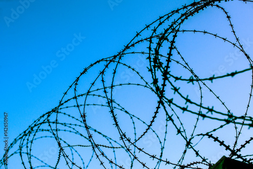 Top of fortress concrete security wall topped with barbed wire against blue sky background - view from prison and  freedom concept 