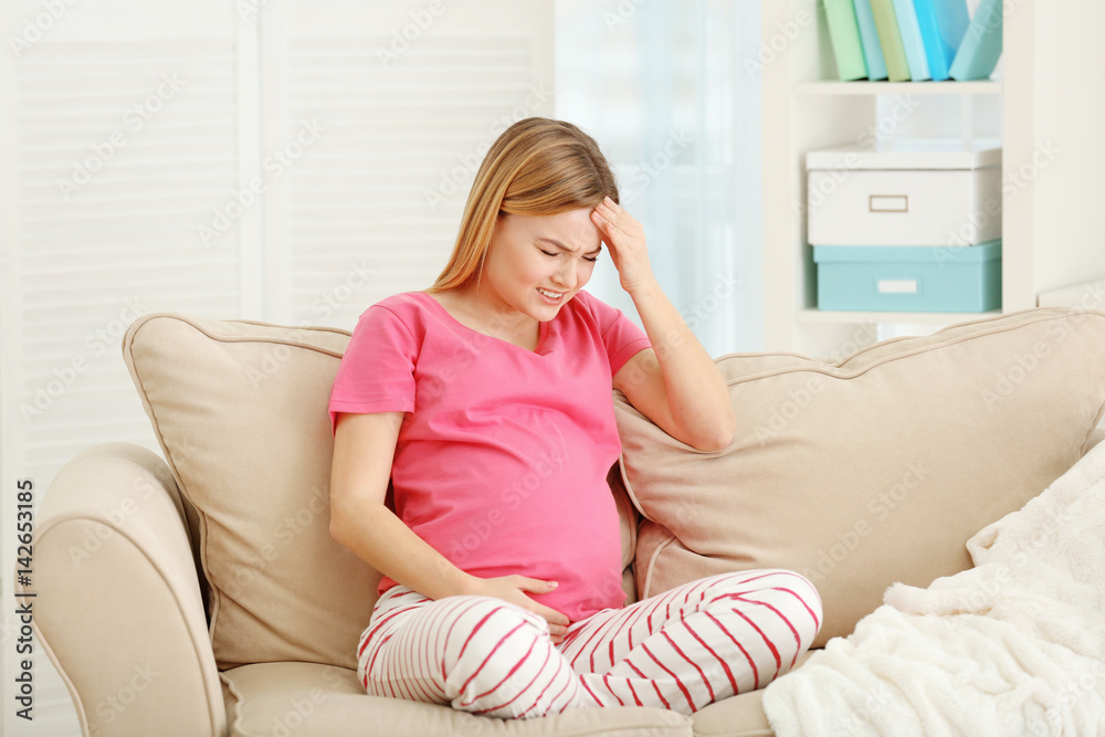 Pregnant woman suffering from headaches while sitting on sofa at home Pregnant woman suffering from headaches while sitting on sofa at home