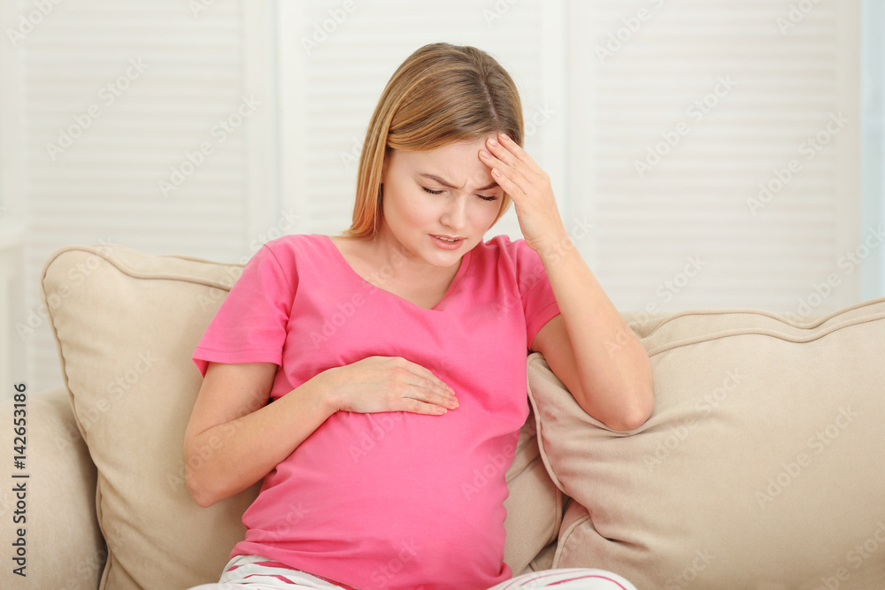 Pregnant woman suffering from headaches while sitting on sofa at home Pregnant woman suffering from headaches while sitting on sofa at home