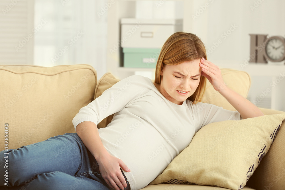 Pregnant woman suffering from headaches while lying on sofa at home Pregnant woman suffering from headaches while lying on sofa at home
